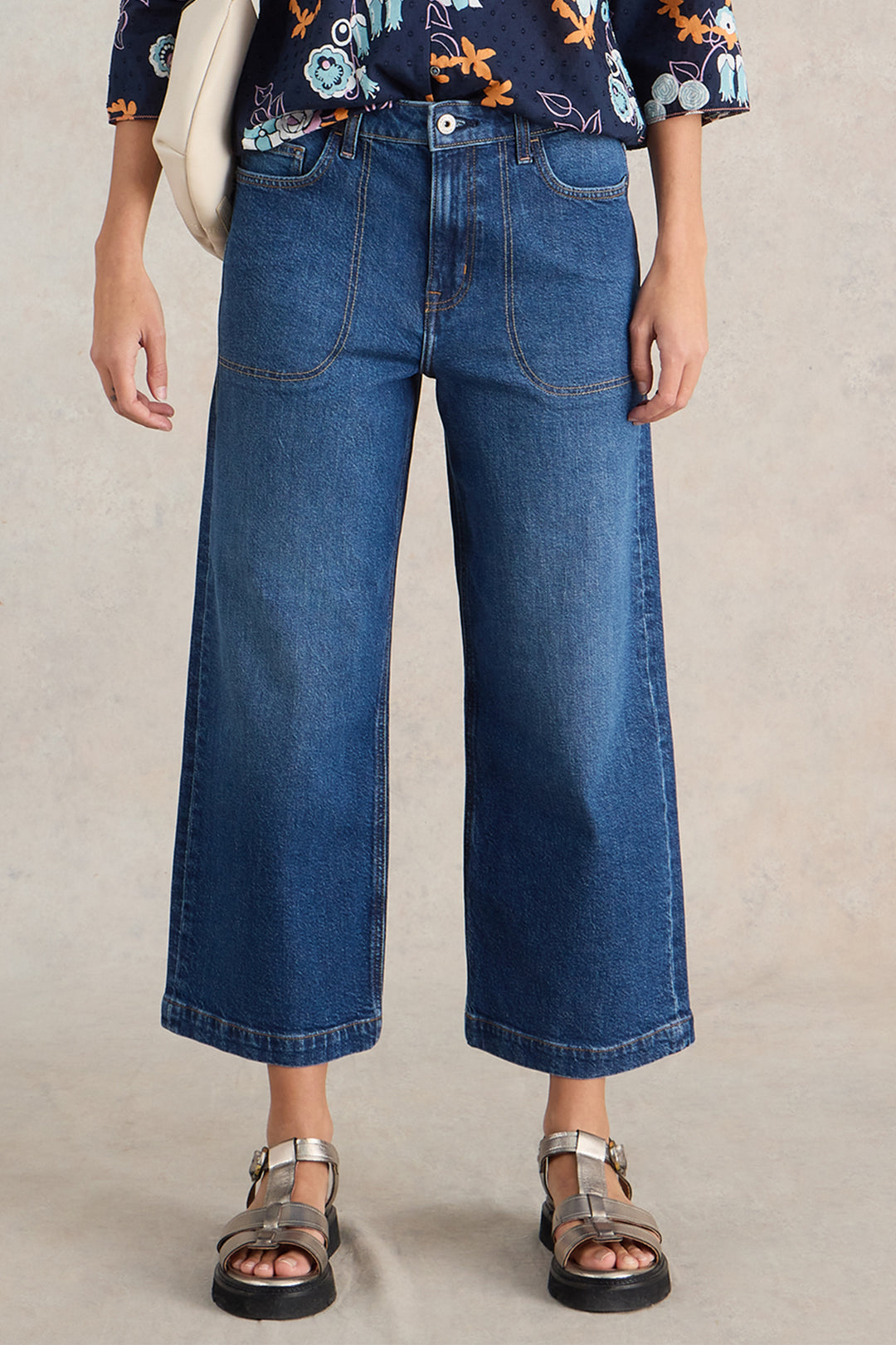 Person wearing blue jeans and a patterned top on a neutral background