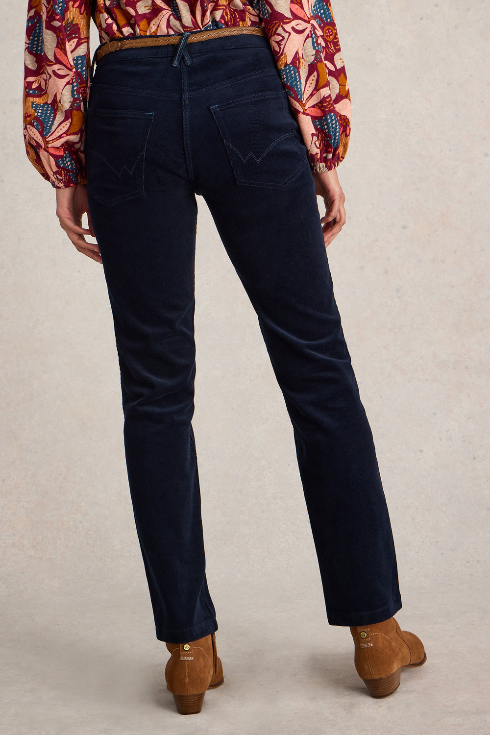 Person wearing navy blue jeans with a patterned top and brown shoes on a neutral background