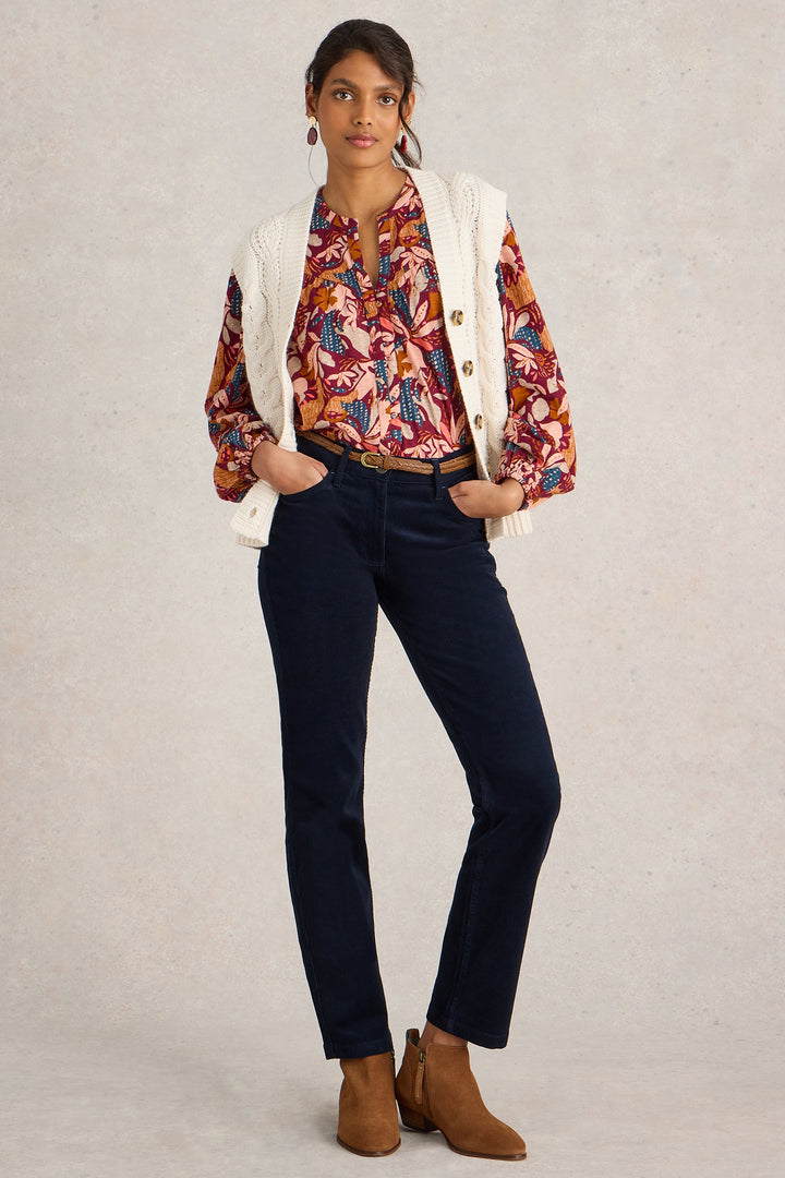 Woman wearing a floral blouse, white cardigan, dark jeans, and brown boots on a plain background
