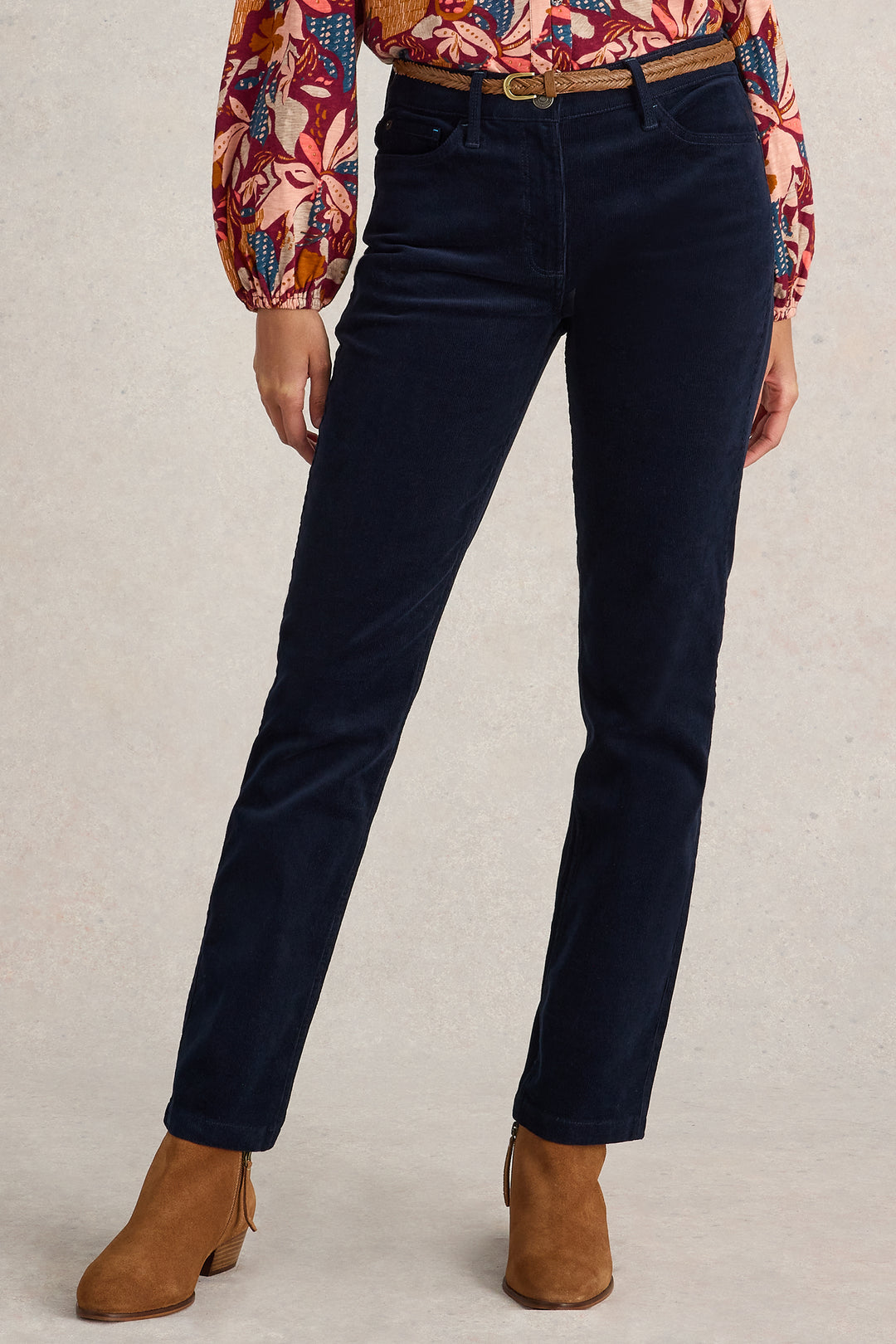Person wearing navy blue pants with a patterned shirt and brown boots on a beige background