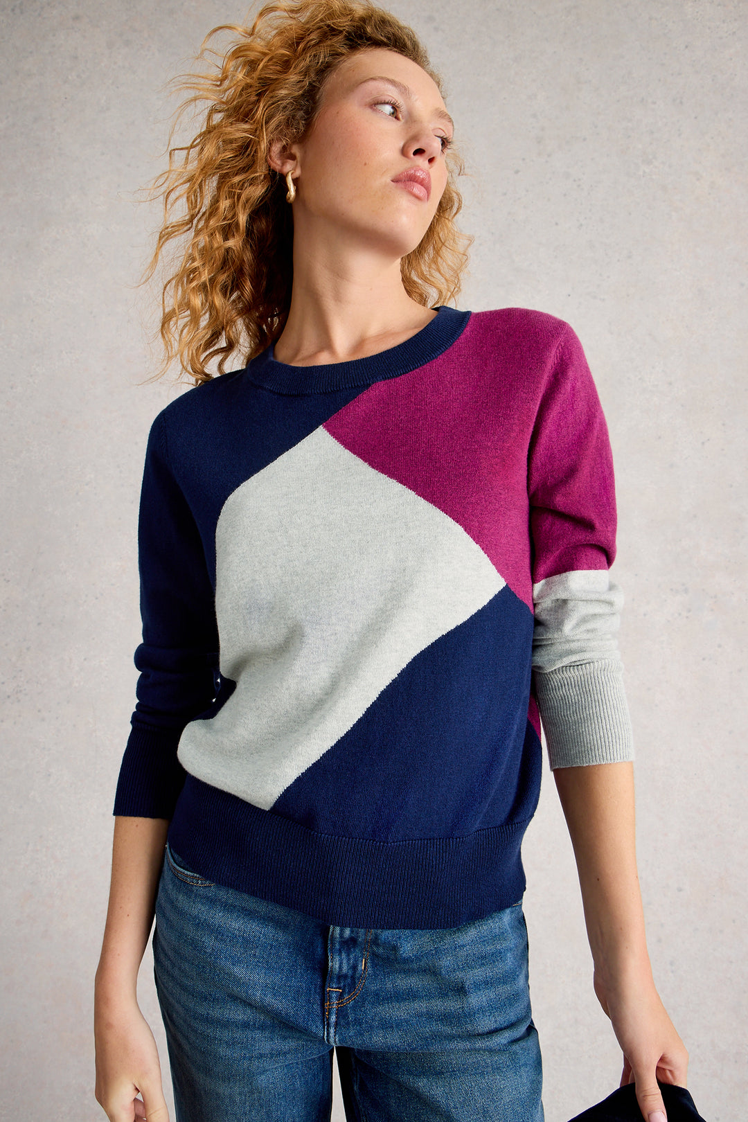 Woman wearing a color-blocked sweater with blue, purple, and gray sleeves against a neutral background