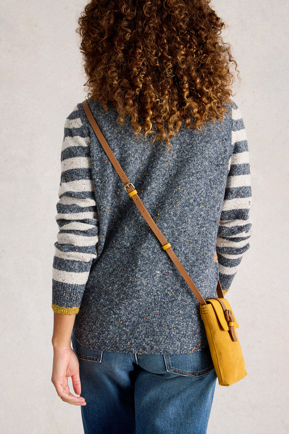 Person wearing a gray and white striped sweater with a yellow bag over one shoulder against a plain background