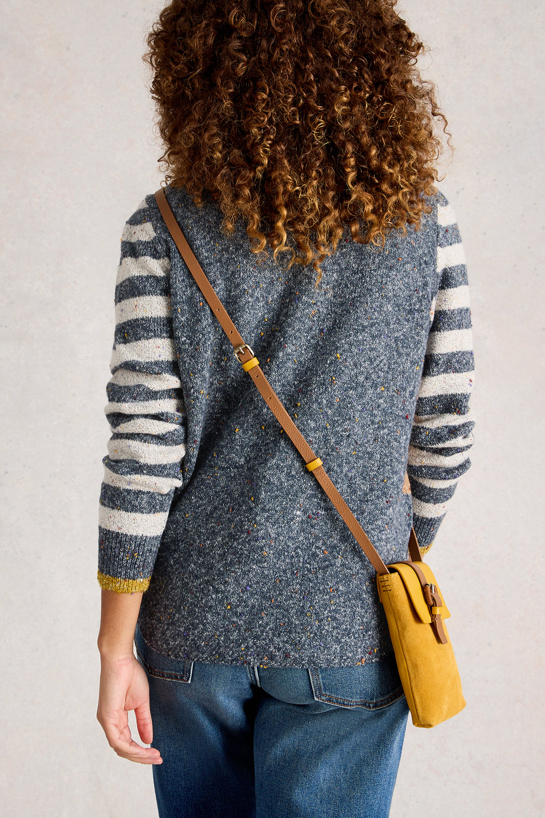 Person wearing a gray and white striped sweater with a yellow bag over one shoulder against a plain background