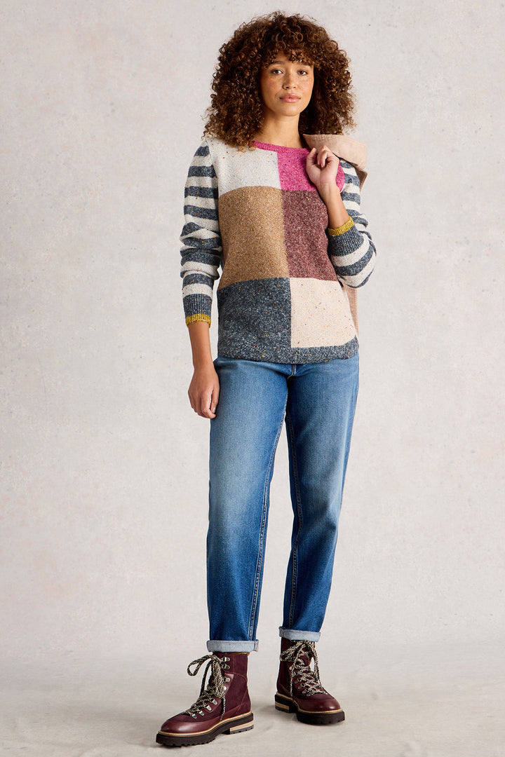 Person wearing a colorful patchwork sweater and blue jeans with brown boots on a plain background