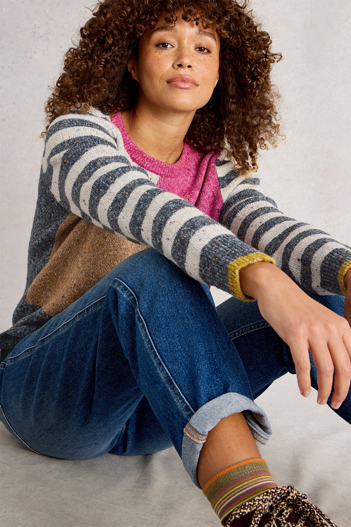 Woman wearing a striped sweater and jeans sitting on a light gray background