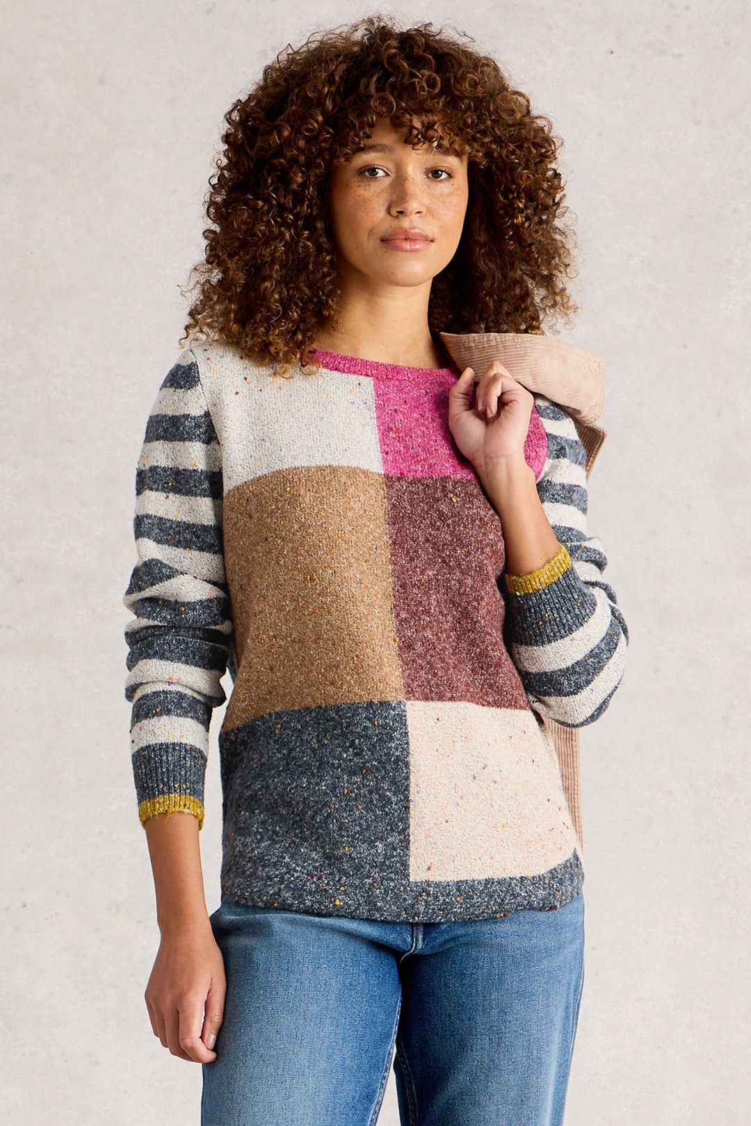 Person wearing a colorful patchwork sweater with a neutral background
