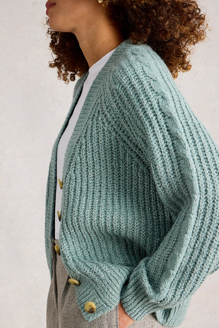Person wearing a teal knitted cardigan with button details on a light background