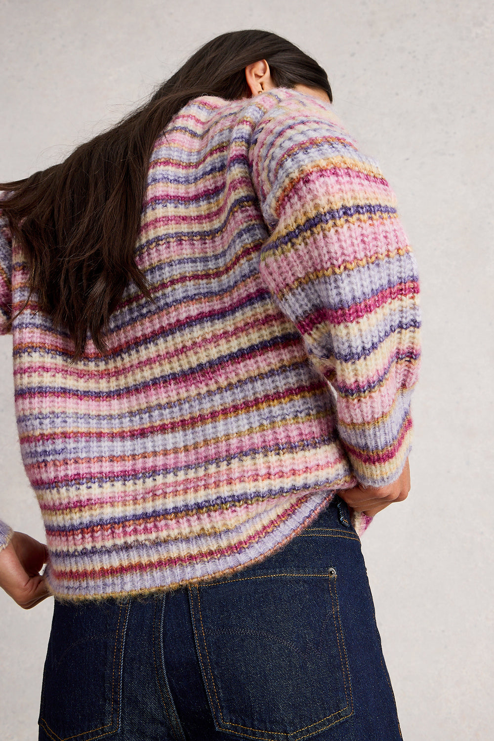 Person wearing a colorful striped sweater from behind on a plain background