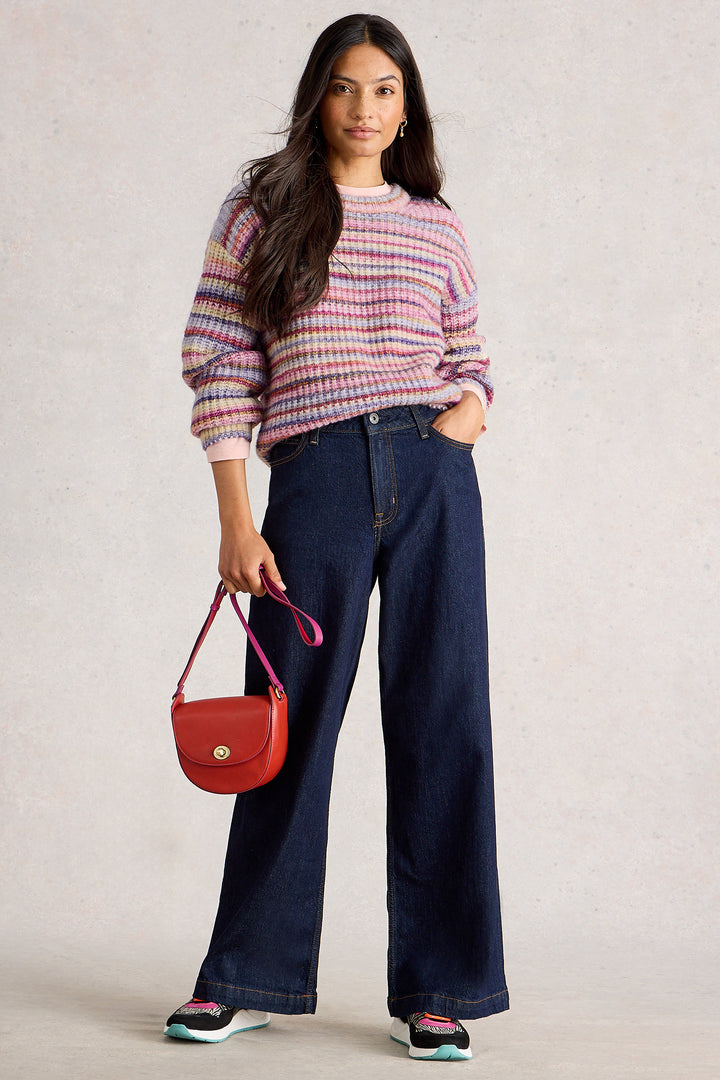 Woman wearing a plaid sweater and blue jeans, holding a red handbag against a plain background