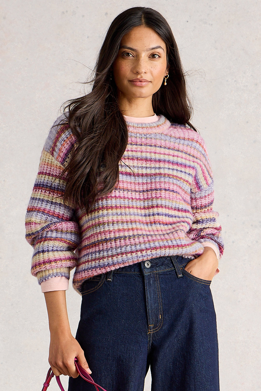Woman wearing a colorful sweater and blue jeans against a plain background