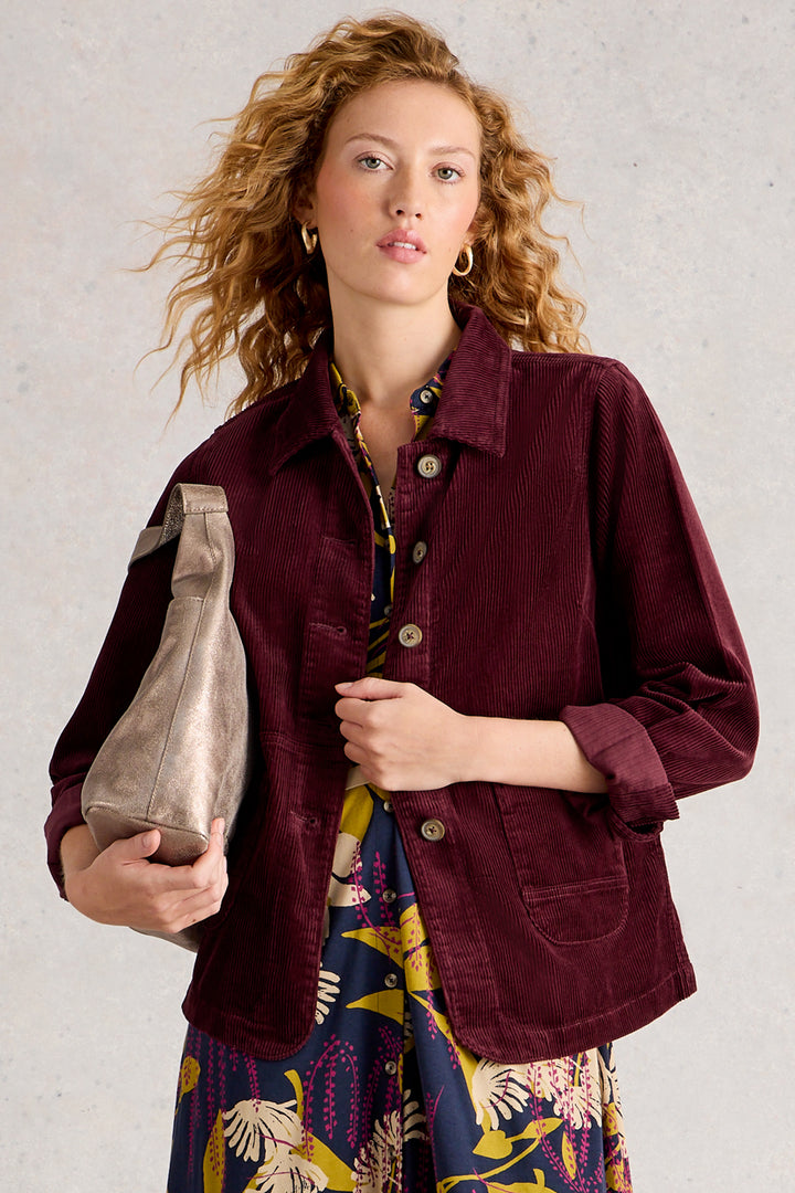 Woman wearing a burgundy jacket over a colorful dress, holding a metallic handbag against a neutral background