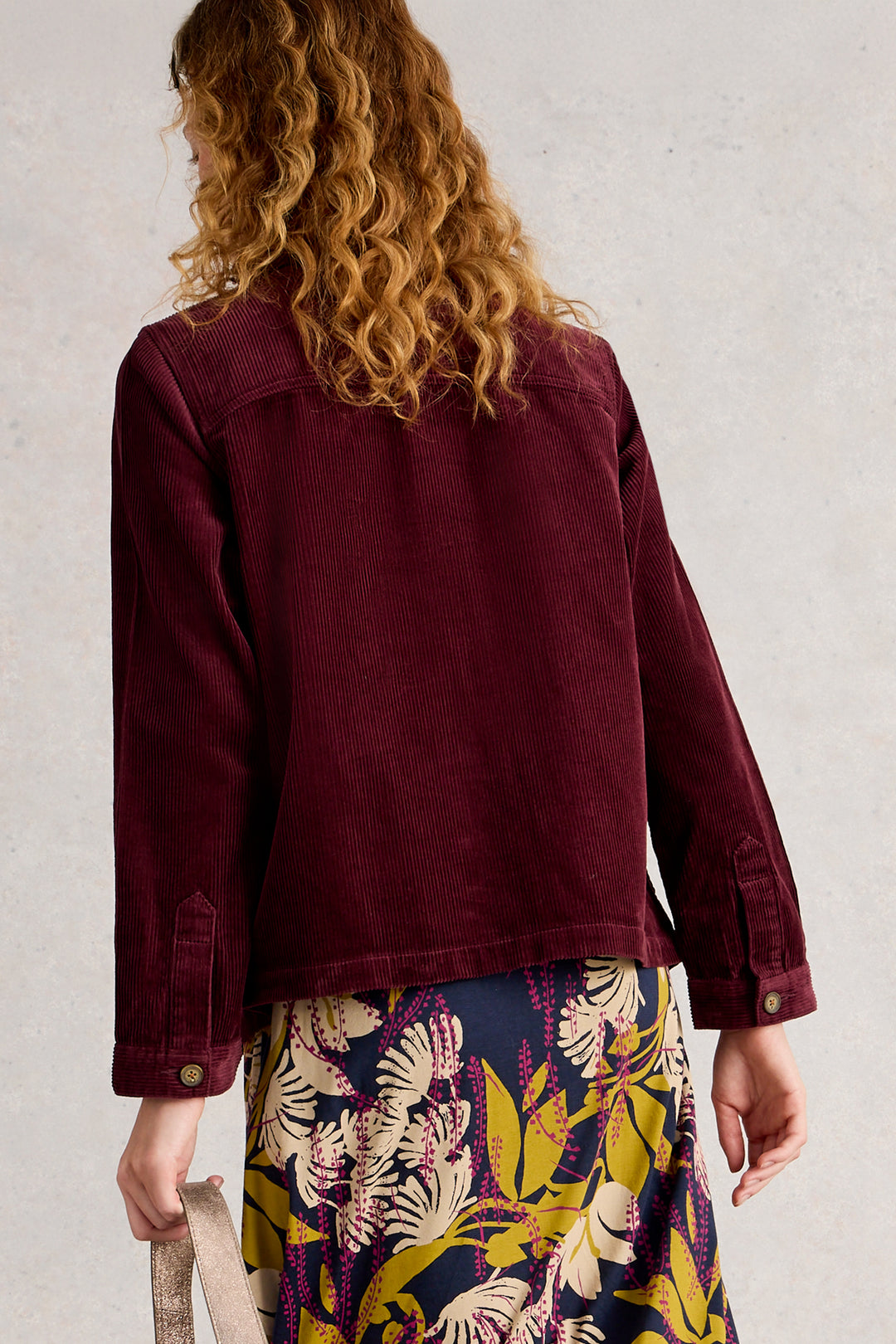 Person wearing a burgundy jacket with a floral skirt against a plain background