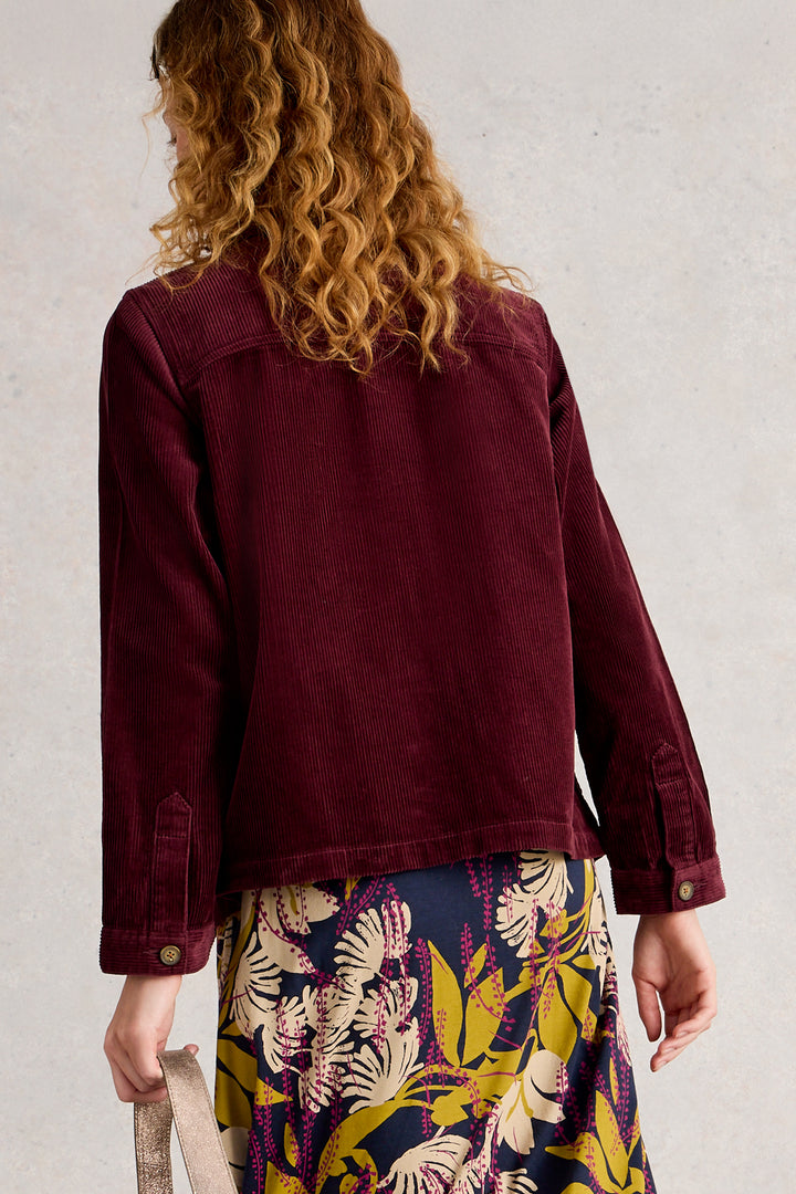 Person wearing a burgundy jacket with a floral skirt against a plain background