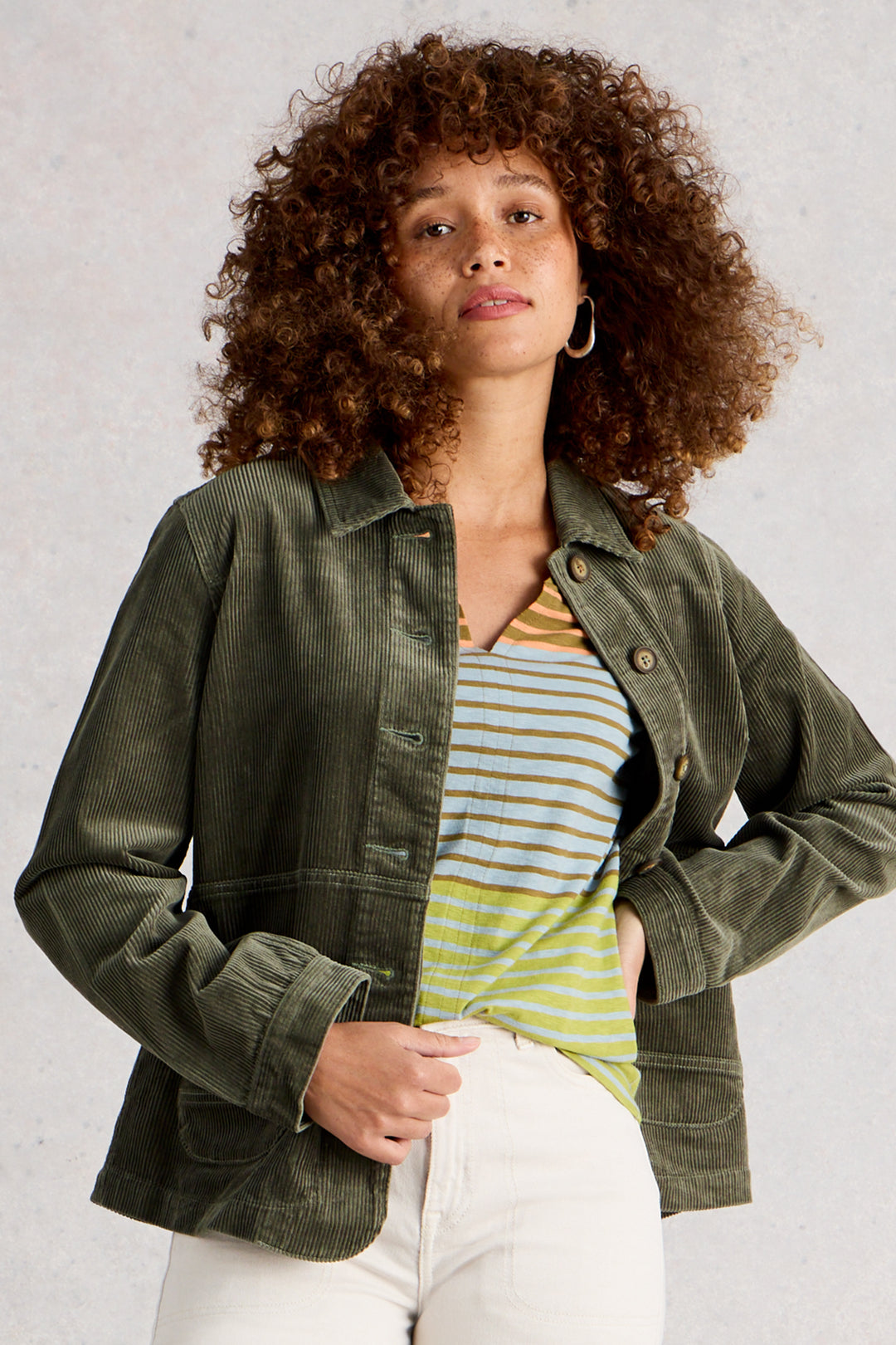 Woman wearing a green jacket over a striped shirt with a neutral background