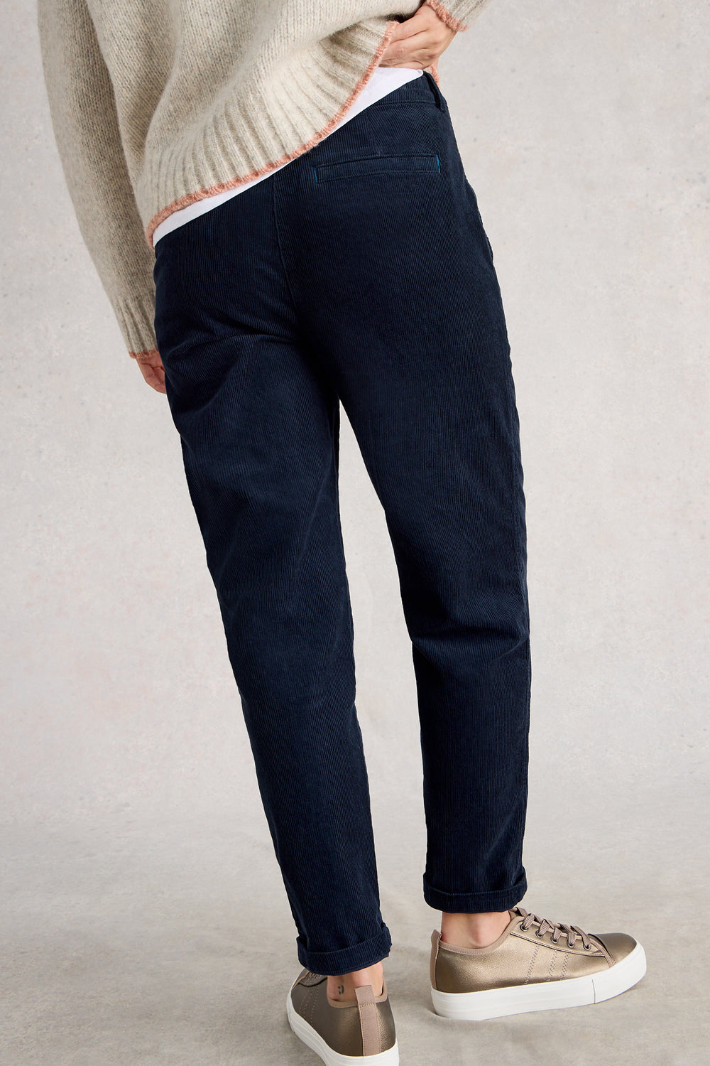 Person wearing navy pants and a beige sweater on a plain background