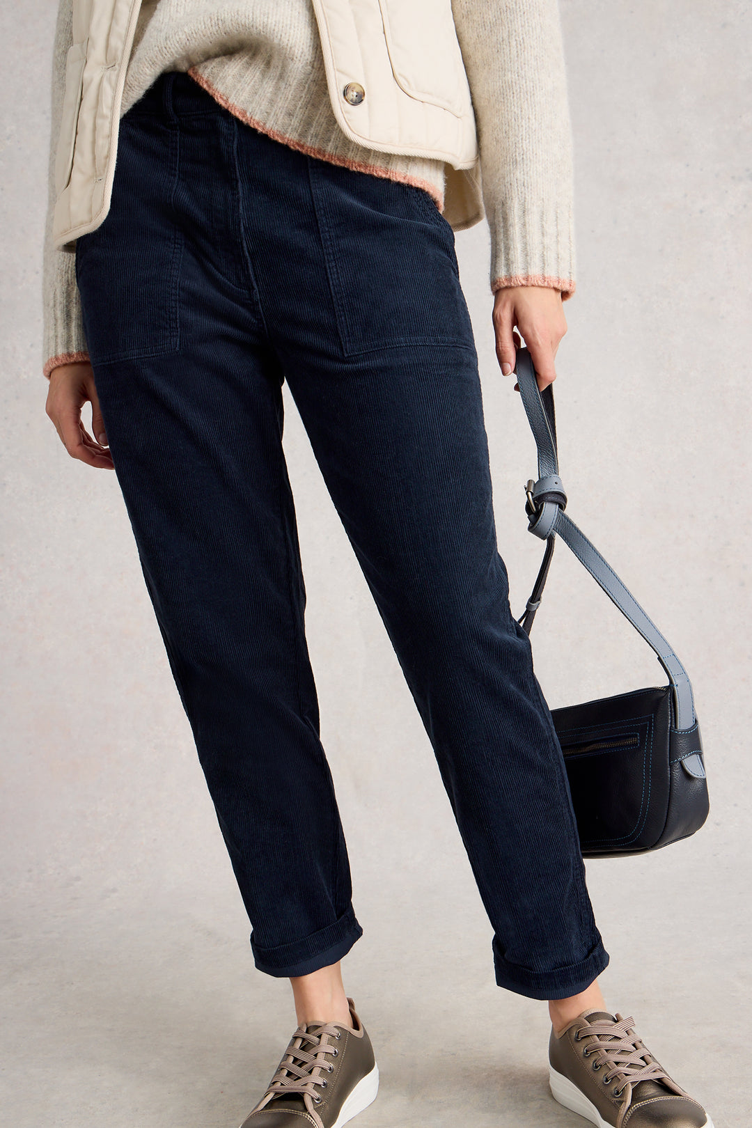Person wearing navy pants and brown shoes, holding a black handbag against a neutral background