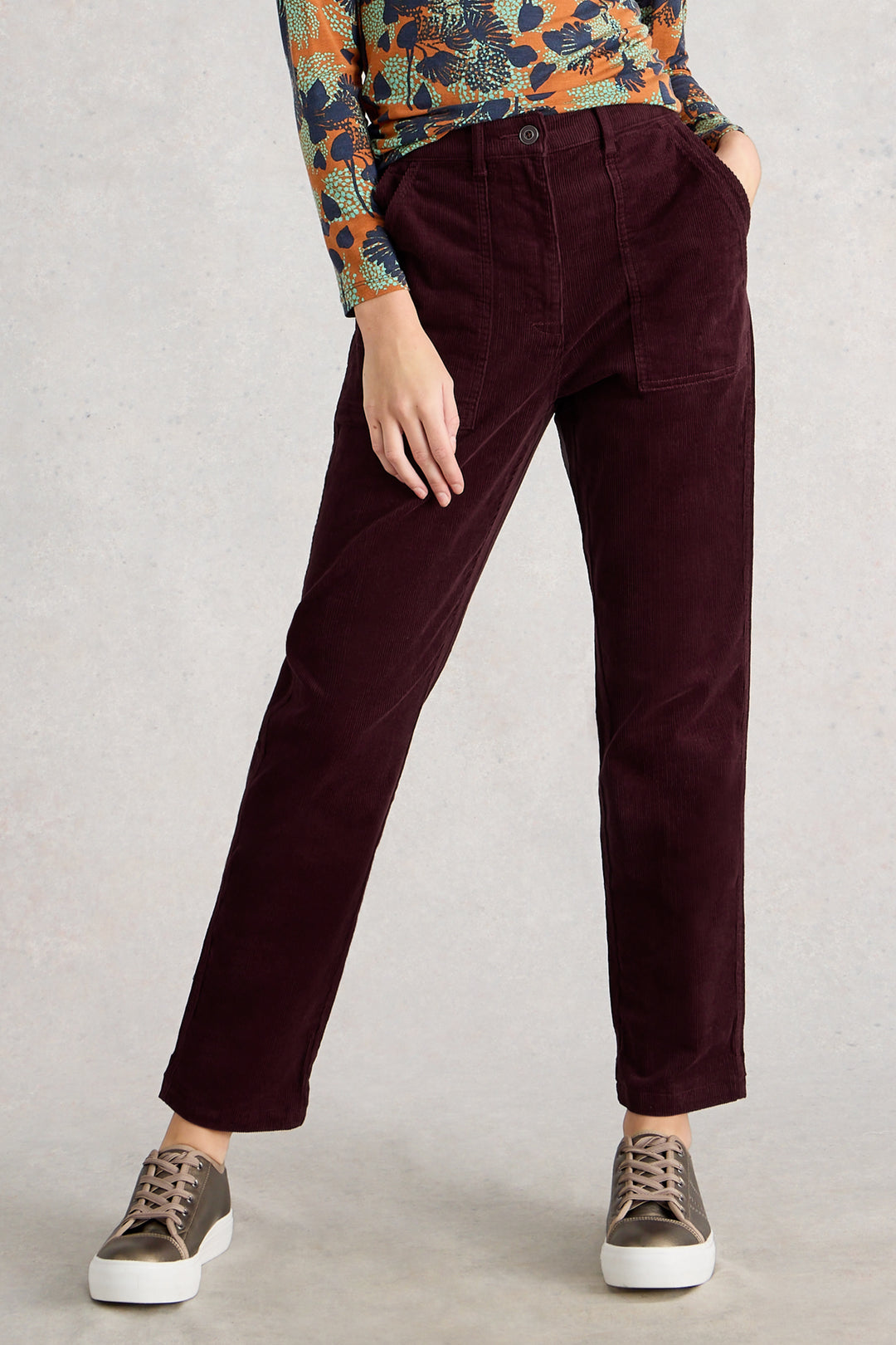 Person wearing burgundy pants with a patterned top and sneakers on a plain background