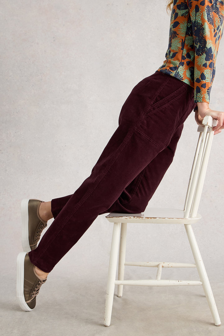 Person wearing burgundy pants and patterned top sitting on a white chair against a plain background