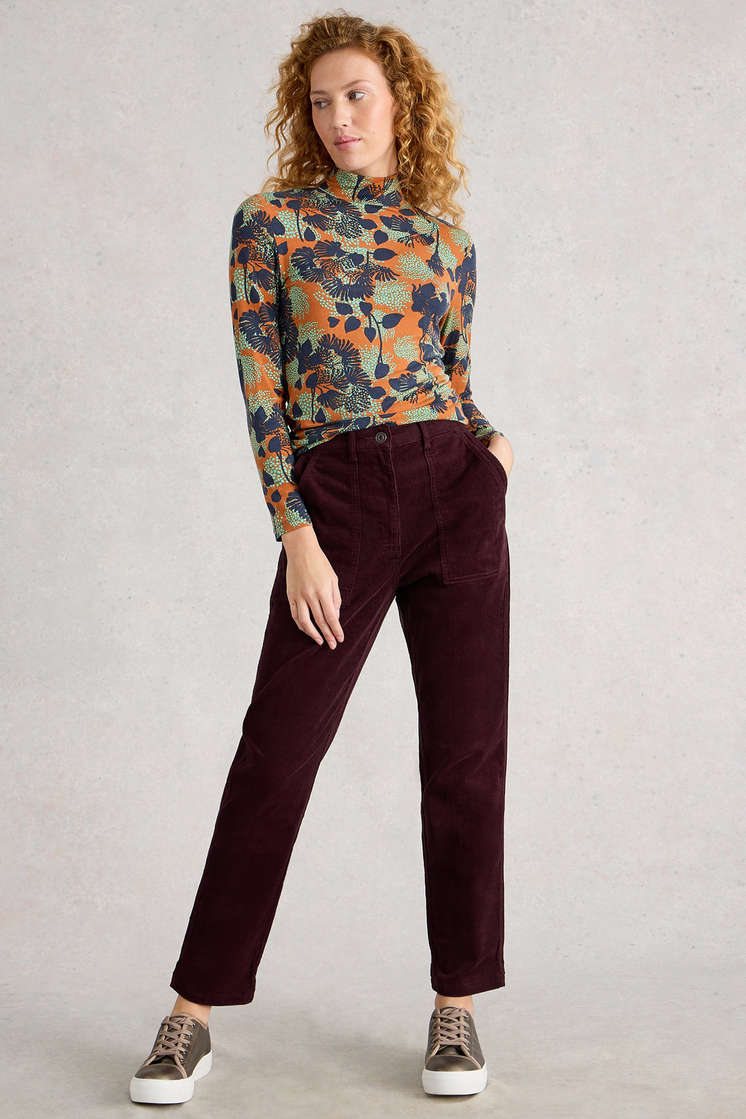 Person wearing a patterned long-sleeve shirt and maroon pants on a plain background