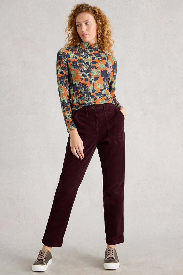 Person wearing a patterned long-sleeve shirt and maroon pants on a plain background