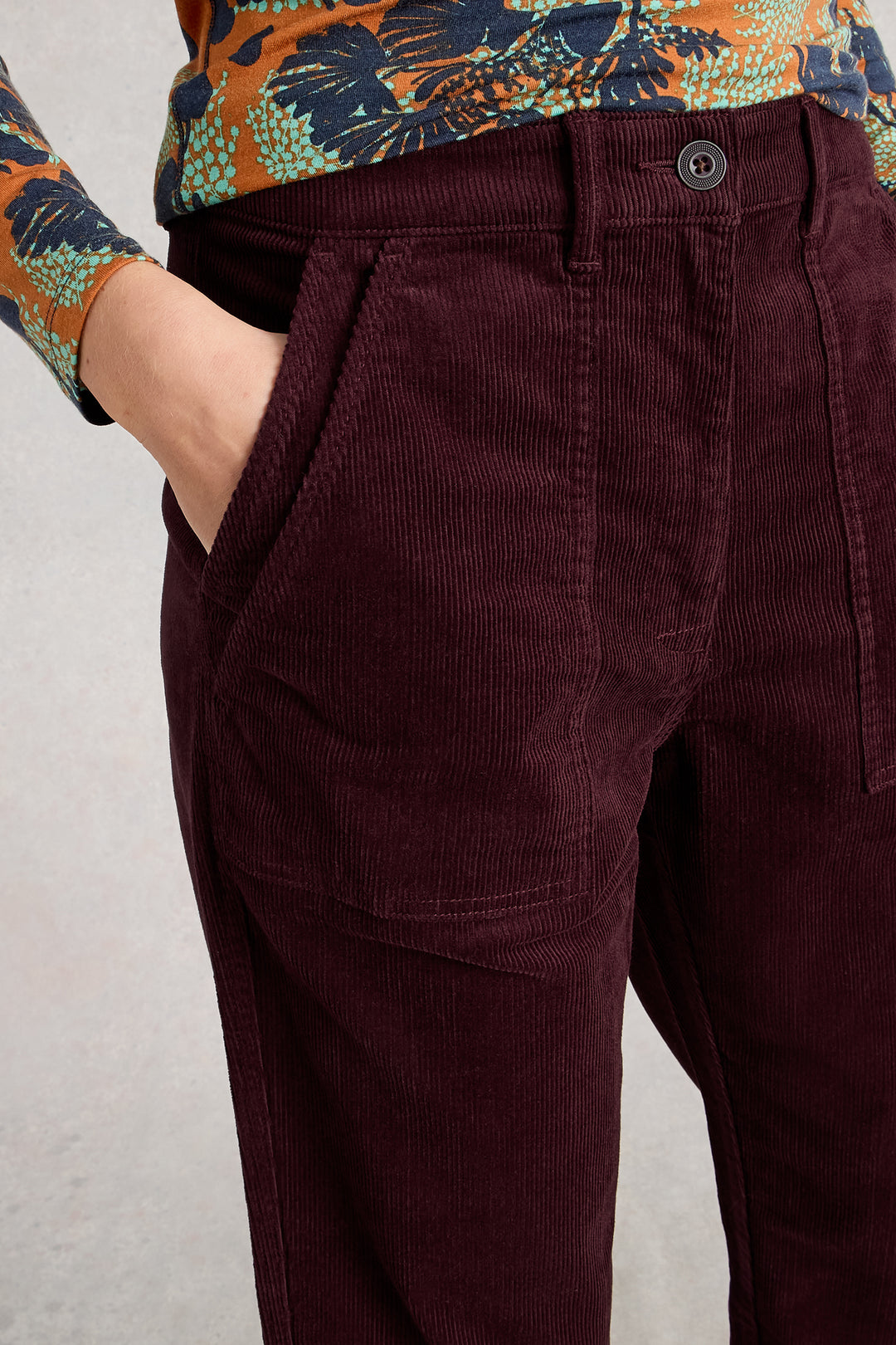 Maroon corduroy pants worn with a floral shirt on a light gray background