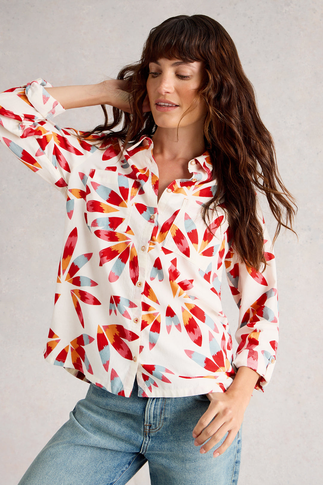 Woman wearing a colorful patterned blouse and jeans against a plain background