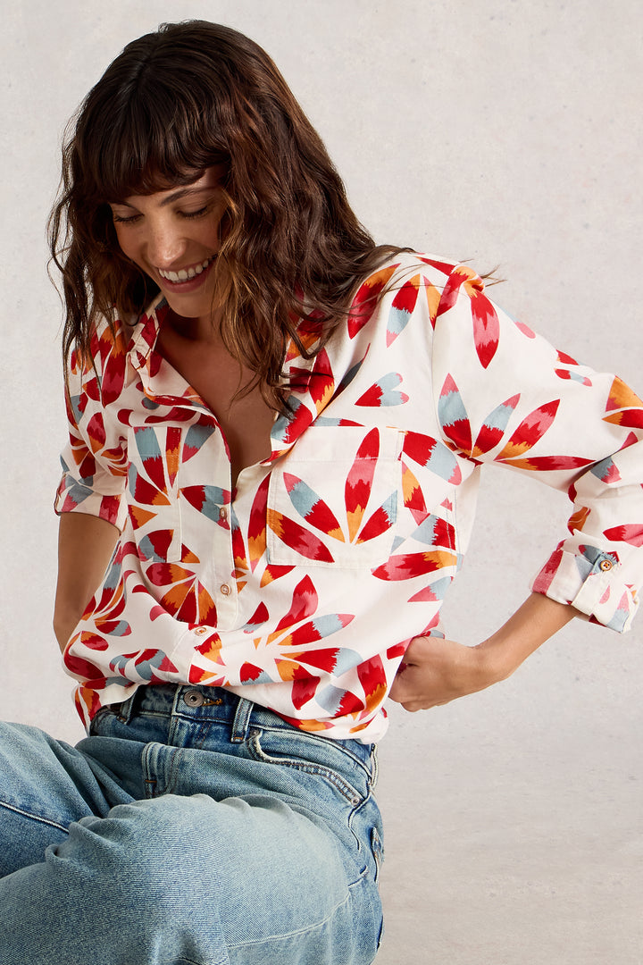 Woman wearing a colorful patterned blouse and jeans against a plain background