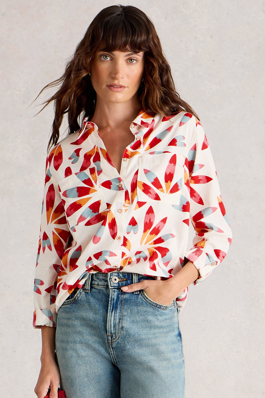 Woman wearing a colorful patterned shirt and jeans against a plain background