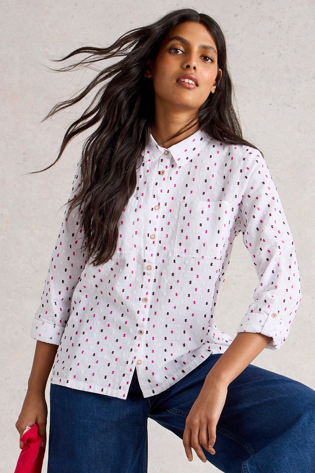 Woman wearing a white blouse with red polka dots and blue jeans against a gray background