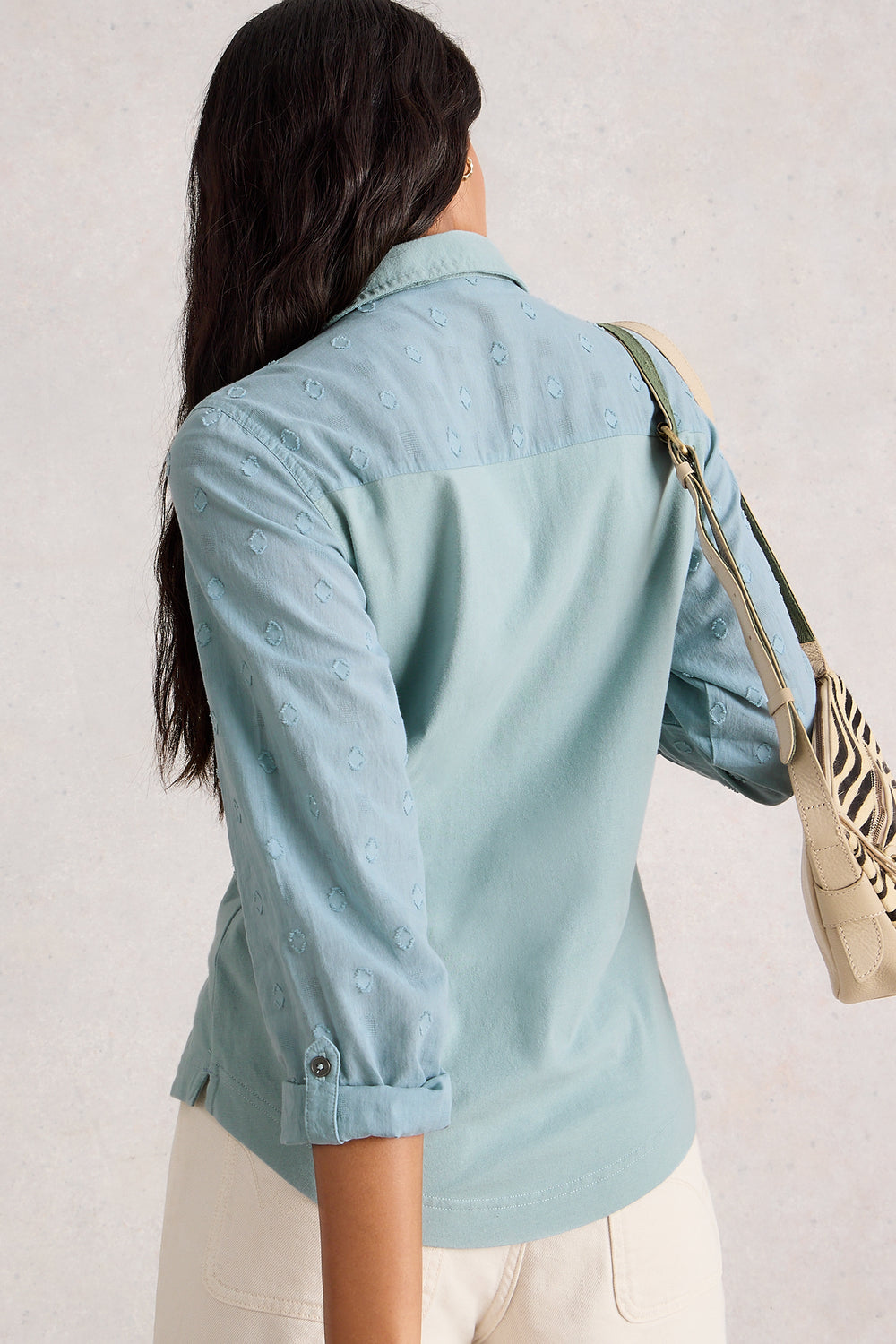 Person wearing a light blue denim jacket with a neutral background