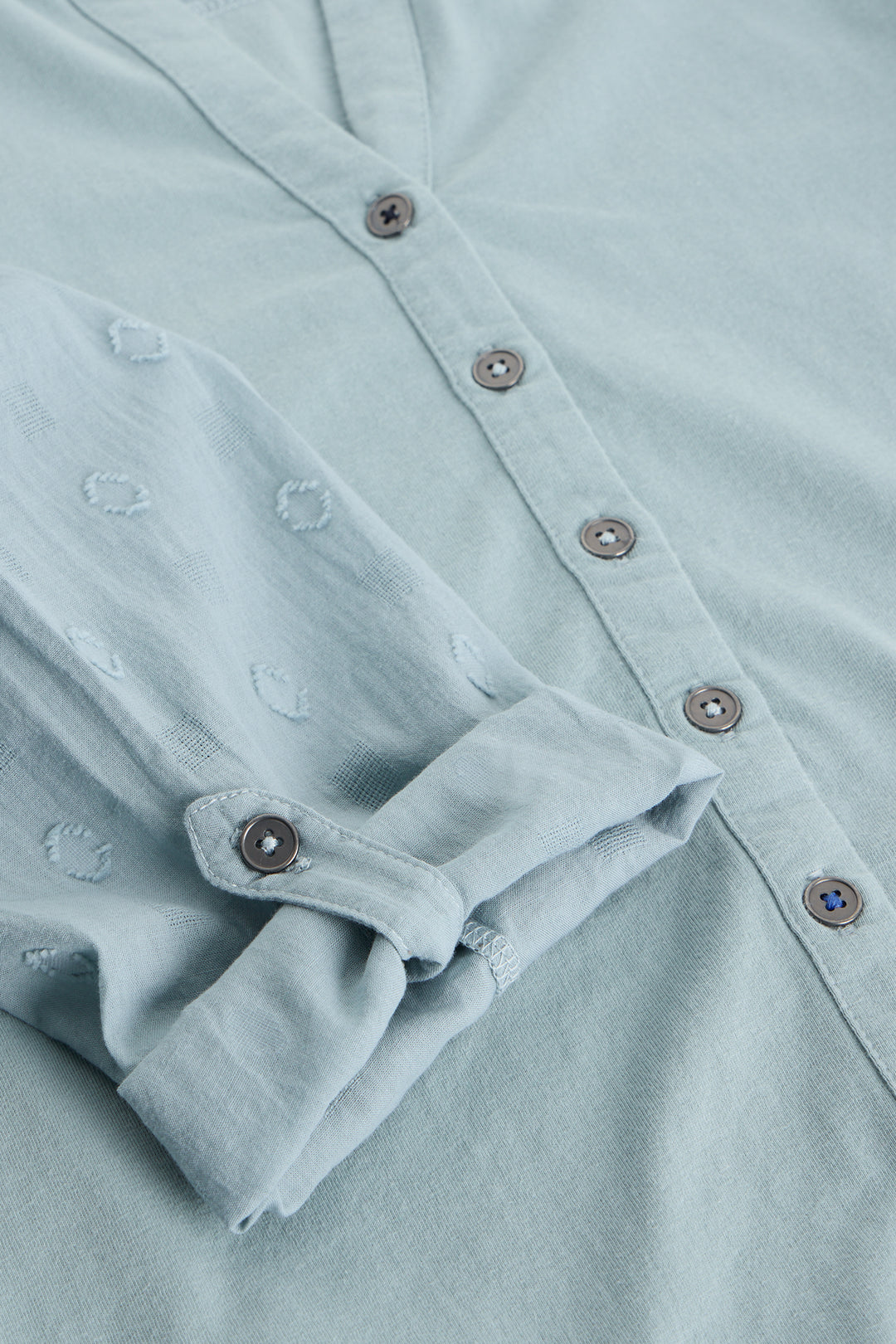 Close-up of a light blue shirt with buttons and rolled-up sleeve