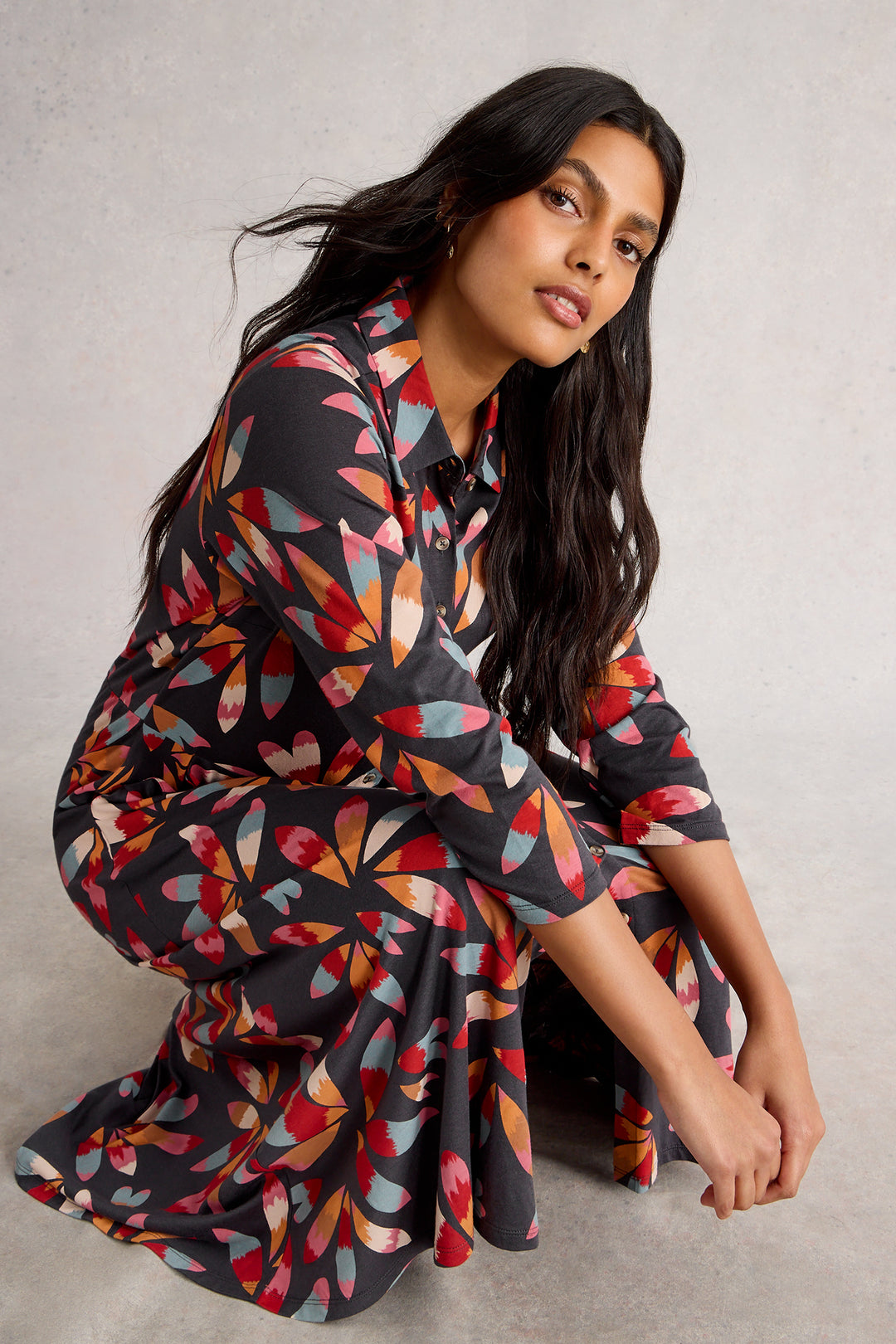 Woman wearing a colorful geometric patterned dress sitting on a gray background