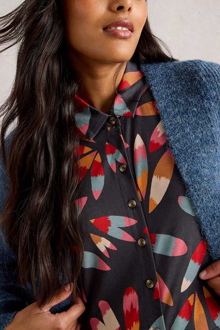 Woman wearing a dark shirt with colorful abstract pattern, holding a blue jacket.