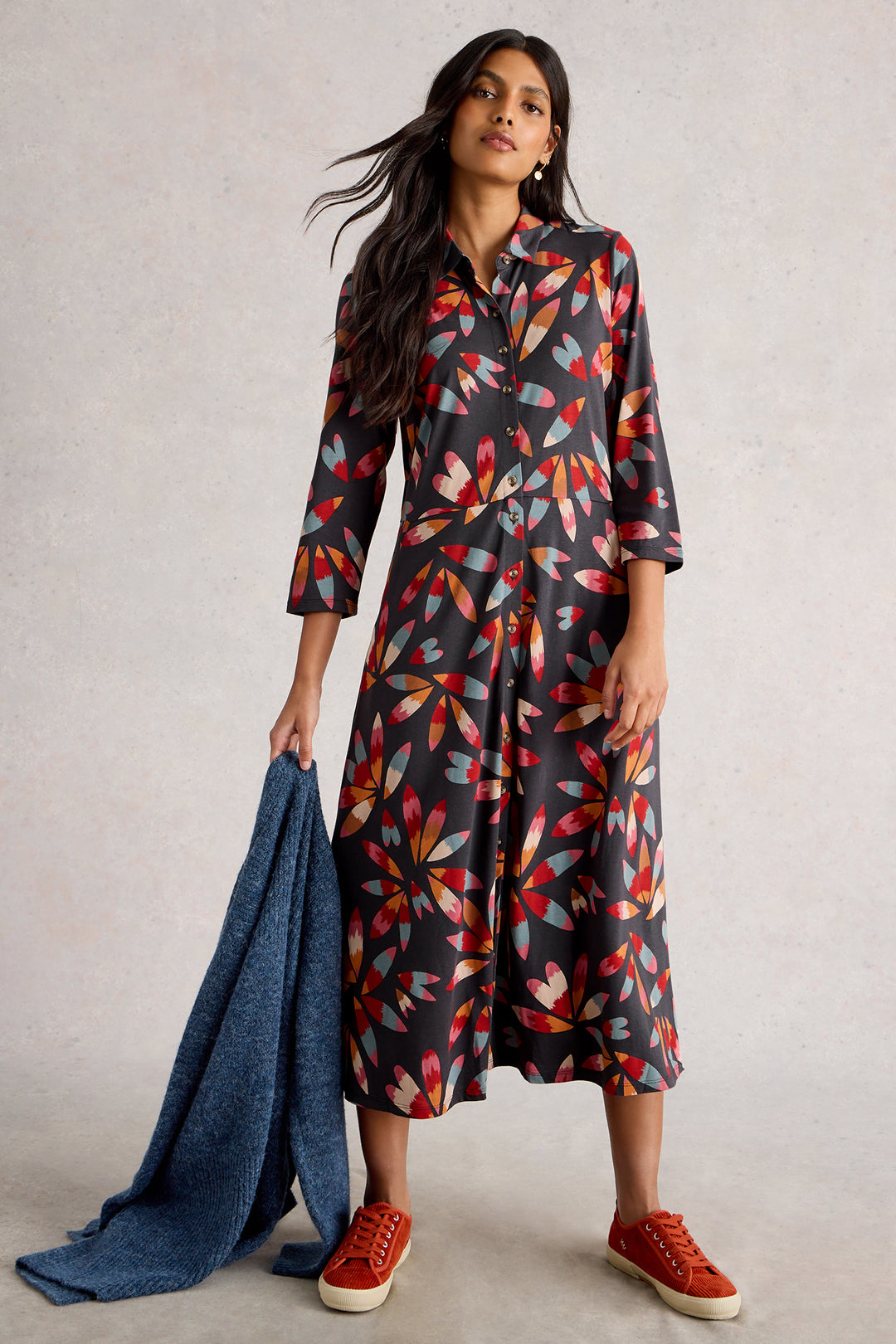 Woman wearing a patterned dress holding a blue scarf against a neutral background