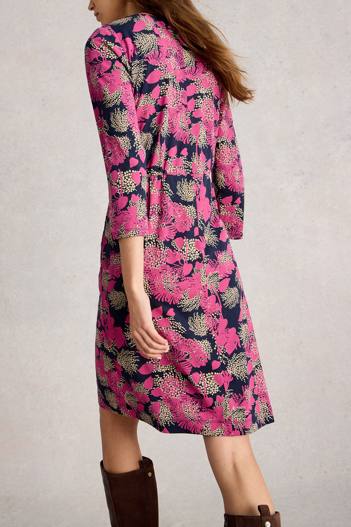Woman wearing a pink floral dress with brown boots on a plain background