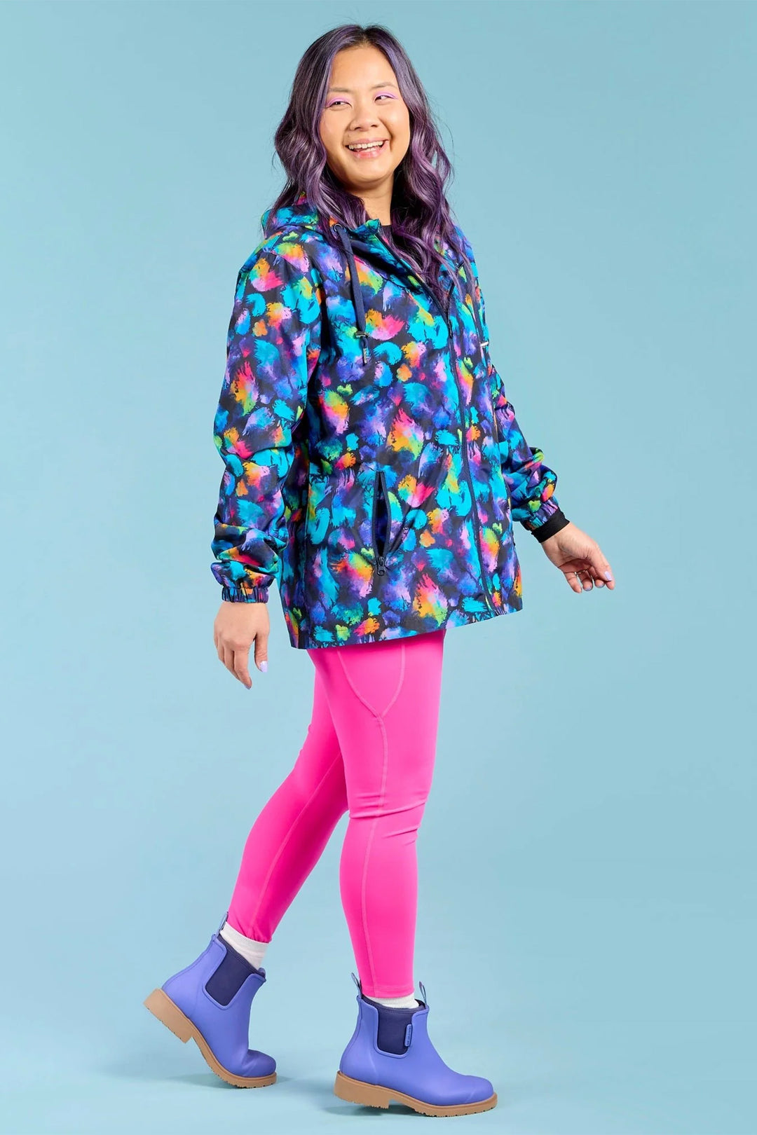 Person wearing a colorful jacket, pink leggings, and purple boots on a light blue background